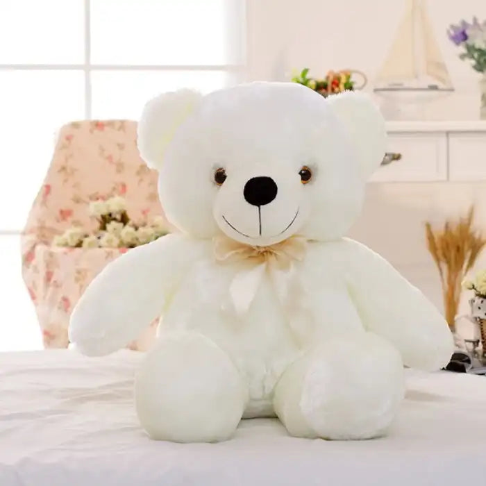 Teddy Bear white plush toy with ribbon sitting on a bed.