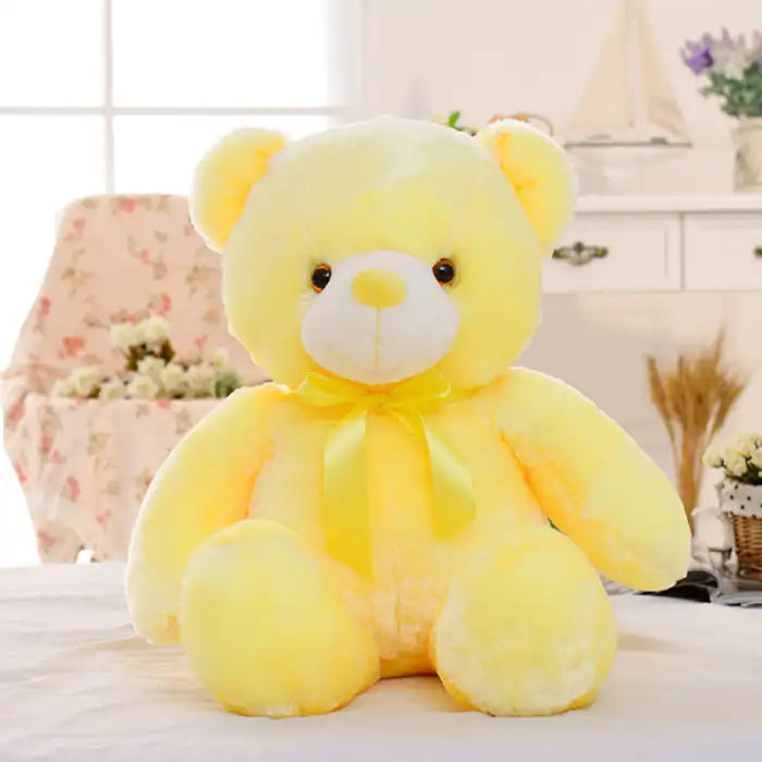 Teddy Bear yellow plush toy with ribbon sitting on a bed indoors.
