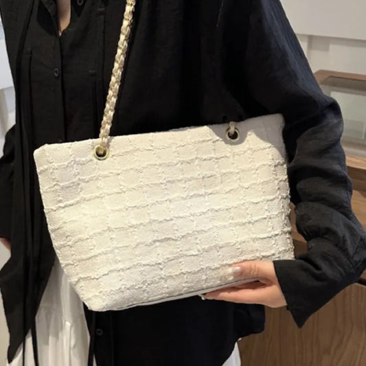 Cream textured handbag with gold chain strap held against black outfit