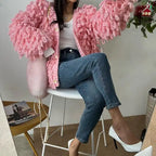 Textured loop knit cardigan jacket in bright pink from seated angle, showcasing voluminous looped sleeve details.