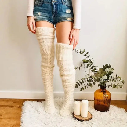 Woman wearing cream knit thigh-high socks, denim shorts, white top, with plant decor and candles on wooden floor