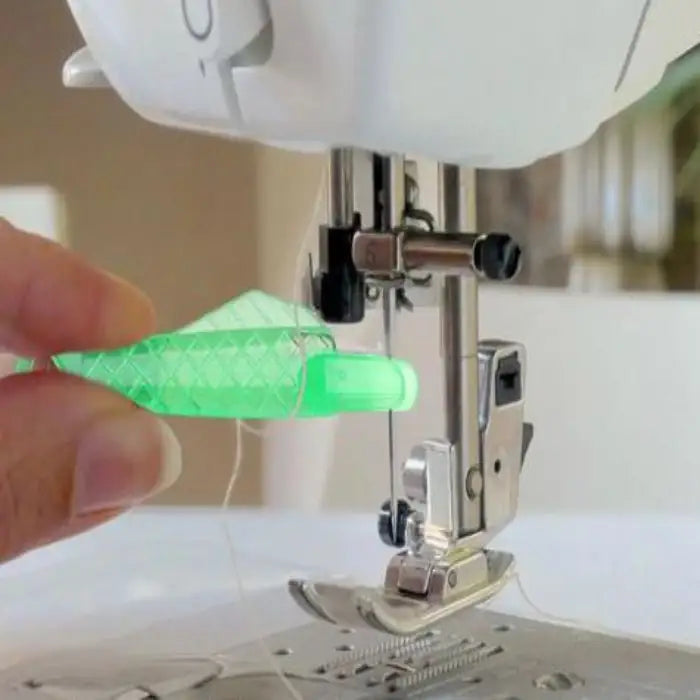 Needle threader used to insert thread through sewing machine needle with fingers holding tool in place