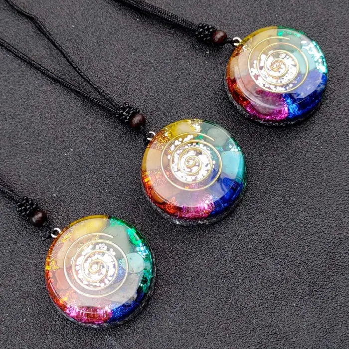 Three chakra healing pendants with rainbow colors and spiral design displayed on black textured surface.