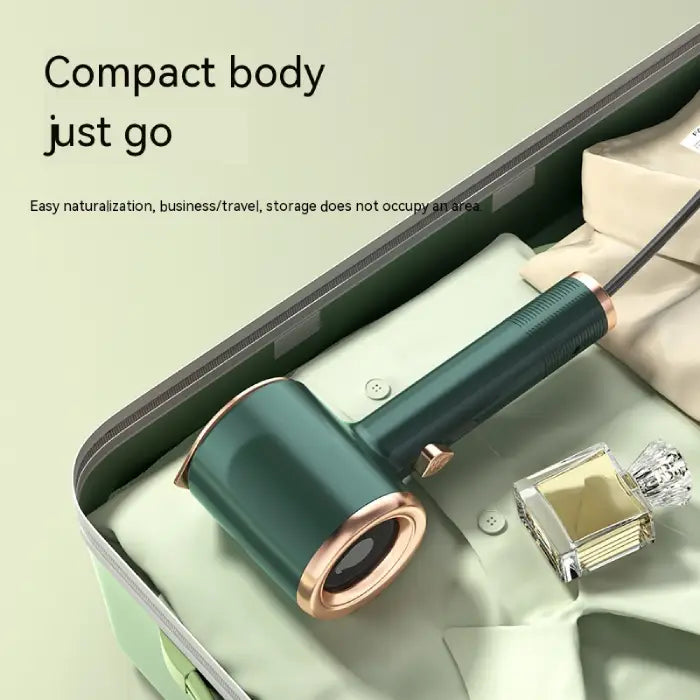 Travel steamer in green fits compactly in suitcase beside folded clothes and perfume bottle.