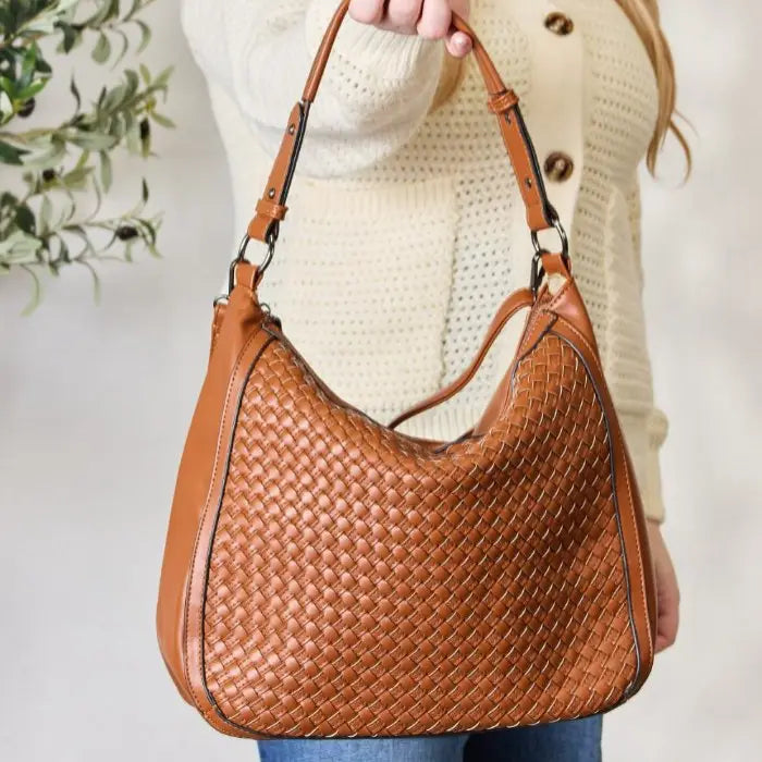 Woman in sweater holding a chic brown woven leather bag.