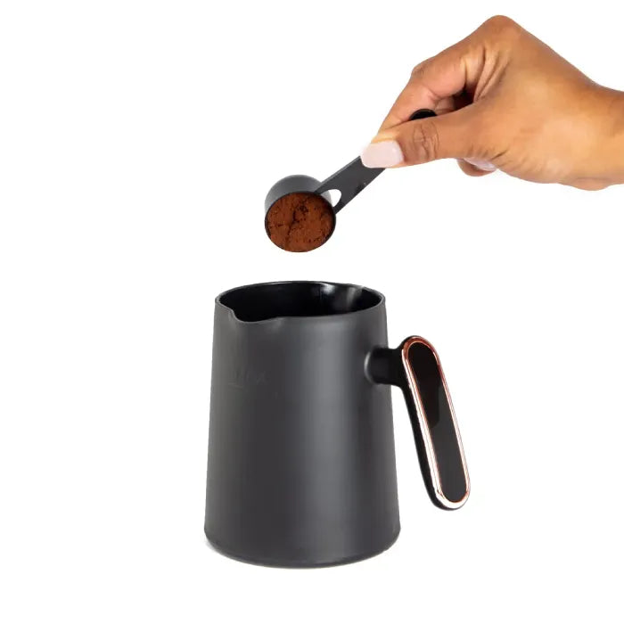 Ground coffee being measured with black serving spoon over coffee pot