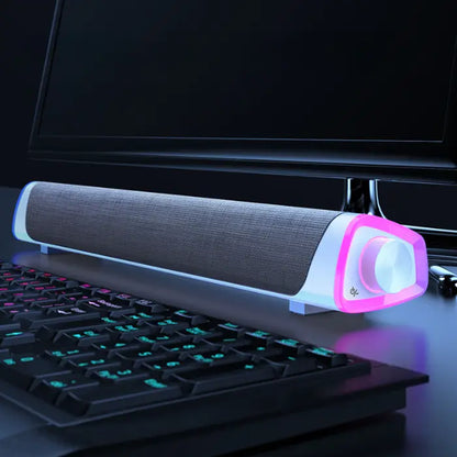 White soundbar with pink LED accent, dual connectivity options, placed in front of a monitor and gaming keyboard