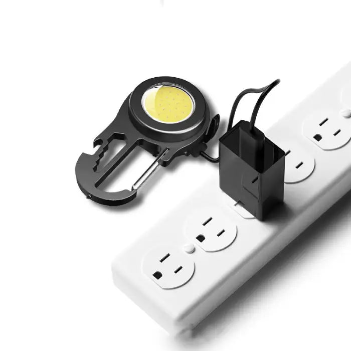  Black COB LED carabiner light being charged via USB adapter on white power strip