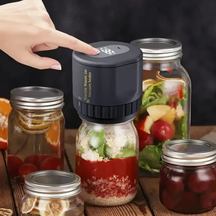 Black electric vacuum sealer on mason jar with layered salad ingredients, surrounded by various jars of preserved foods on wooden surface