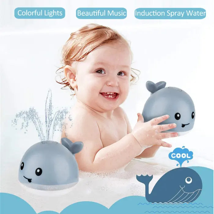 Happy baby in bathtub holding whale bath toy while another one sprays nearby.