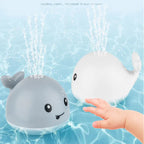 Baby reaching for gray and white whale bath toys spraying water in pool.