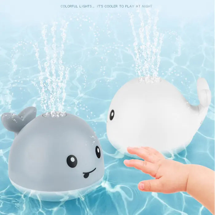 Baby reaching for gray and white whale bath toys spraying water in pool.