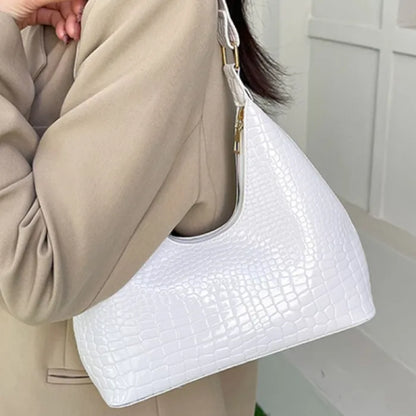 Person wearing beige outfit holding white crocodile-embossed shoulder bag with gold hardware