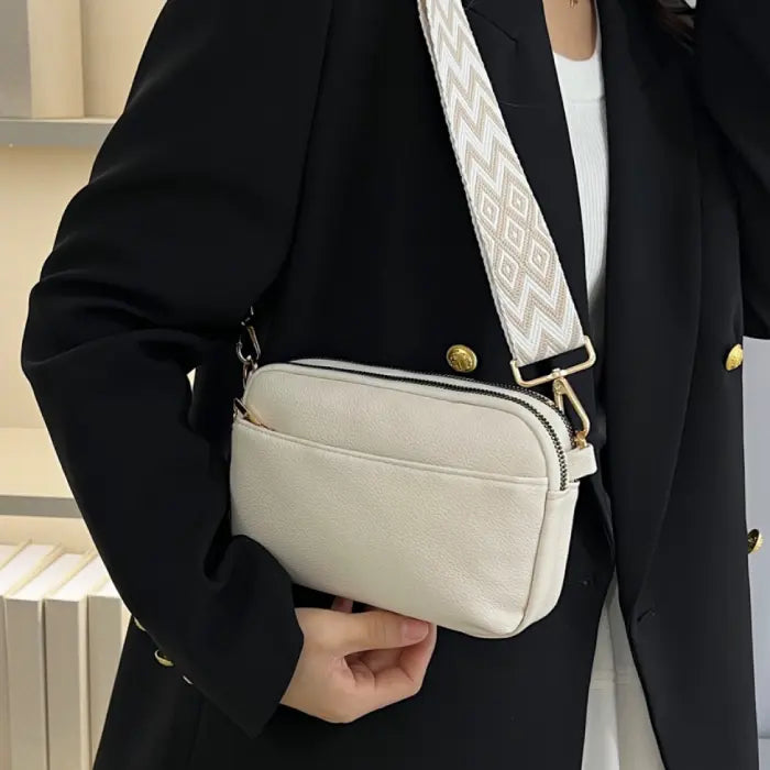 White crossbody bag with a chevron strap styled with a blazer, perfect for professional and elegant looks.