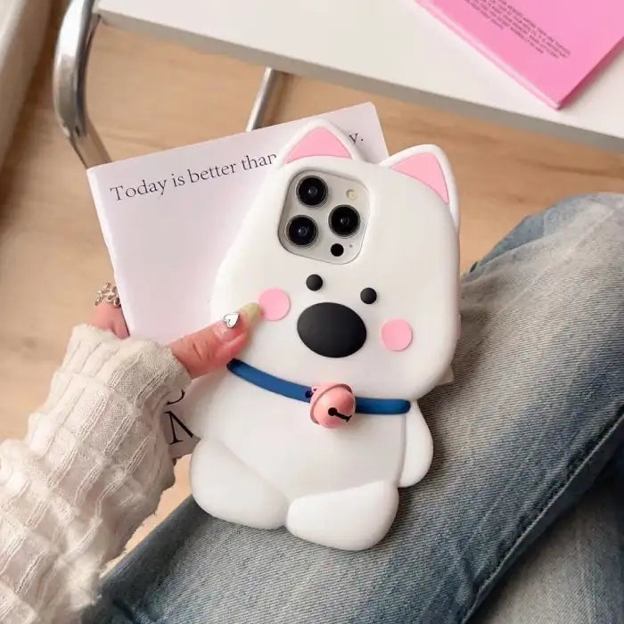 white dog phone case with pink ears, a blue collar, and a pink bell, resting on a person's lap.