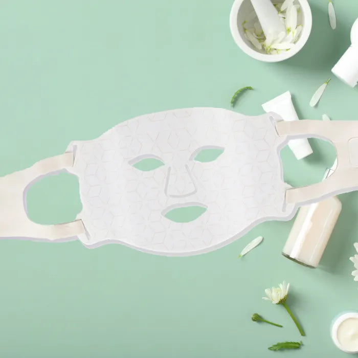 White geometric facial mask on green background with skincare products.