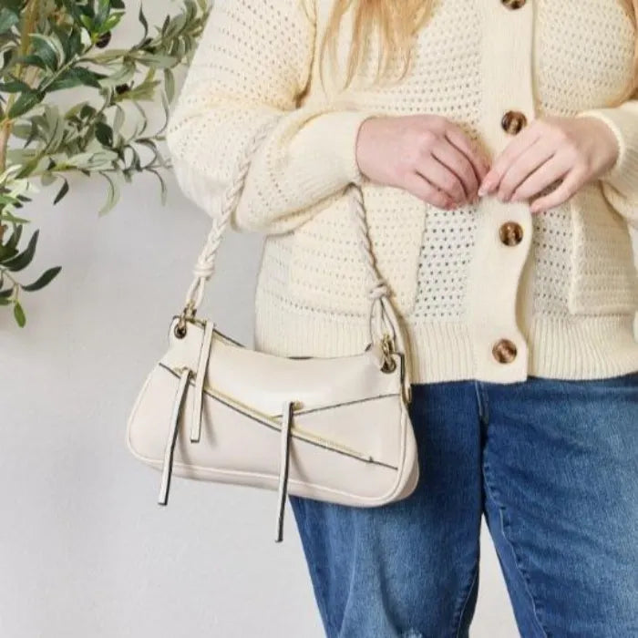 Close-up of cream leather handbag showing diagonal zipper details and braided handle against neutral background