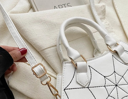 White handbag with spiderweb design, showing gold adjustment buckle on strap