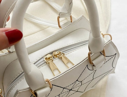 Close-up of white handbag with spiderweb design, showing smooth gold zipper closure