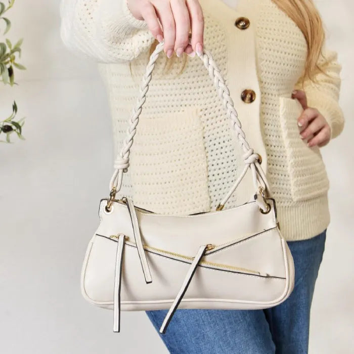 Cream leather shoulder bag featuring braided handle, gold hardware accents and decorative front zipper details