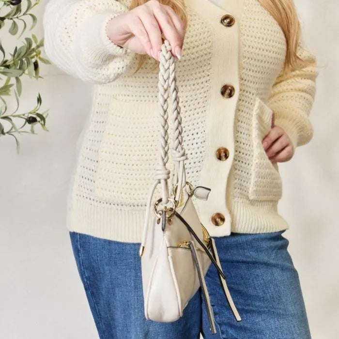 Detailed view of cream handbag's braided leather handle and decorative hanging tassels with gold hardware elements