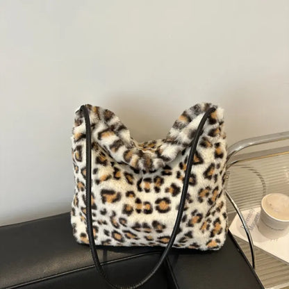 White leopard print faux fur handbag with a black strap placed stylishly on a black sofa.