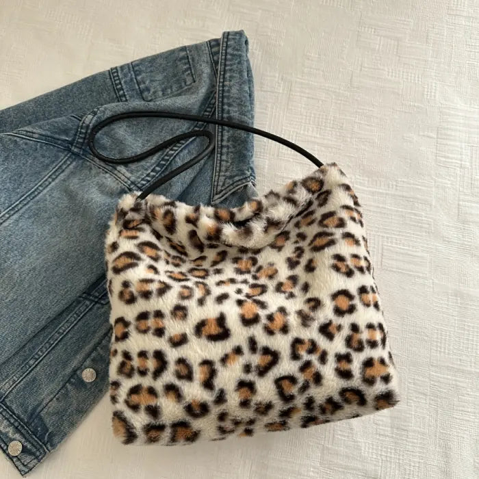 White leopard print faux fur handbag with black strap, styled next to denim for a casual outfit.