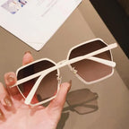 Designer white metal geometric sunglasses with gradient brown lenses casting stylish shadow on neutral surface