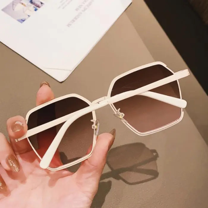 Designer white metal geometric sunglasses with gradient brown lenses casting stylish shadow on neutral surface