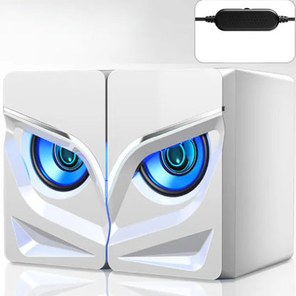 White computer speakers with owl-like blue glowing eyes, angular design, and USB controller on blue background