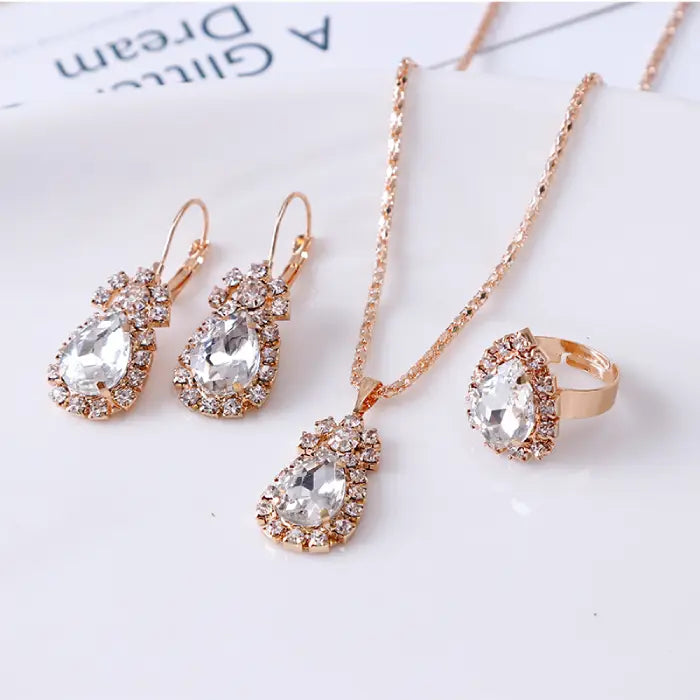 White teardrop gemstone jewelry set with necklace, earrings, and ring in gold surrounded by crystals.