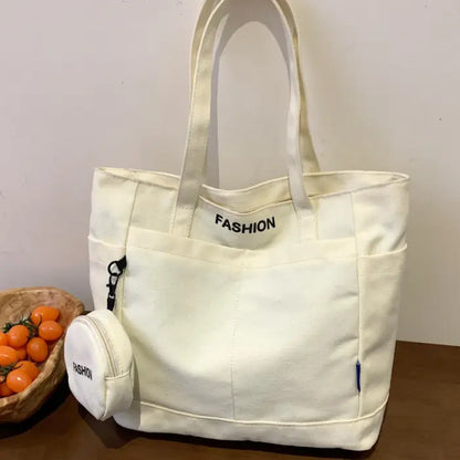 Elegant white tote bag with mini pouch labeled "Fashion," displayed on a table beside fresh tomatoes.