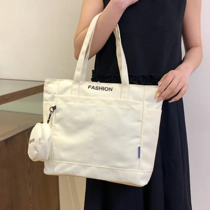 White tote bag with mini pouch carried by a woman in a black dress, perfect for casual outfits.