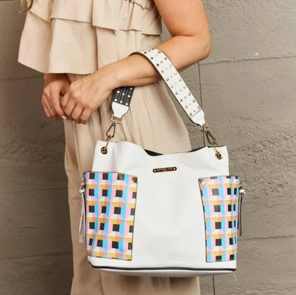 White shoulder bag with pastel geometric panels and studded strap, displayed against textured wall