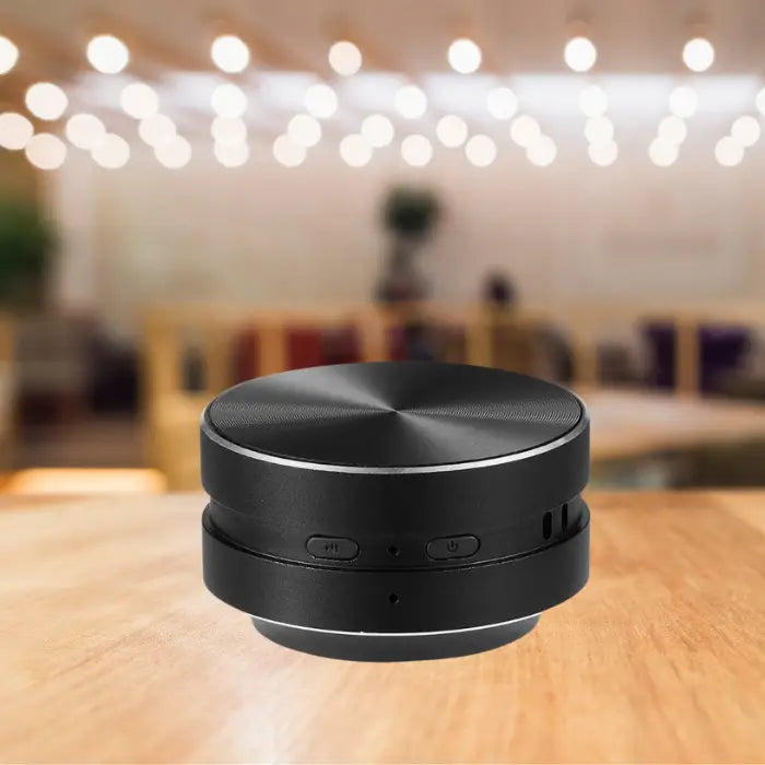 wireless bluetooth speaker in sleek black design displayed on wooden table with ambient lighting and bokeh effect