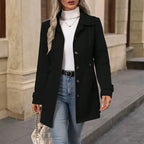 Woman wearing a black coat, white turtleneck, and blue jeans standing on a street.