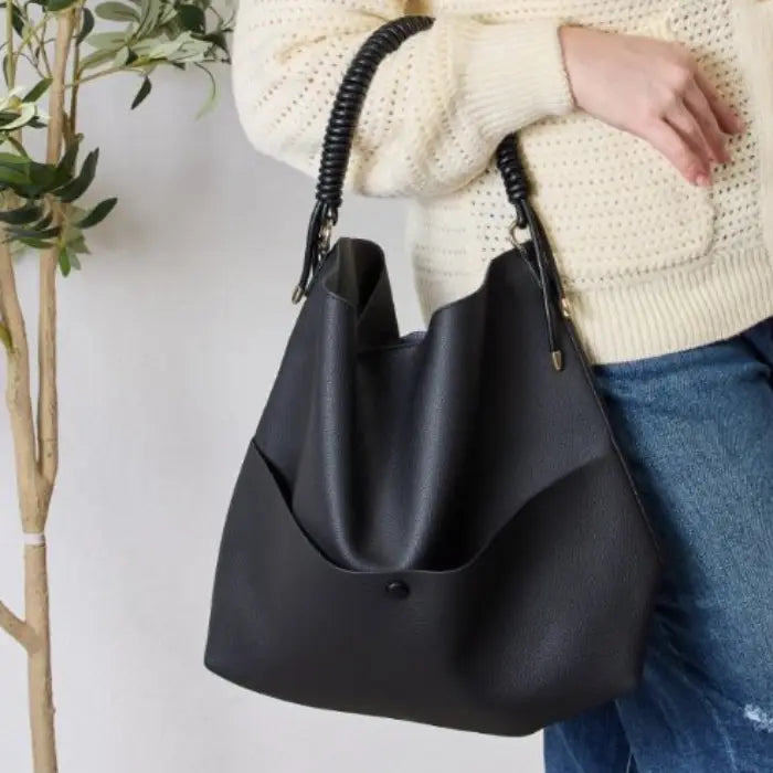 Woman holding black handbag with coiled handle wearing cream sweater and jeans