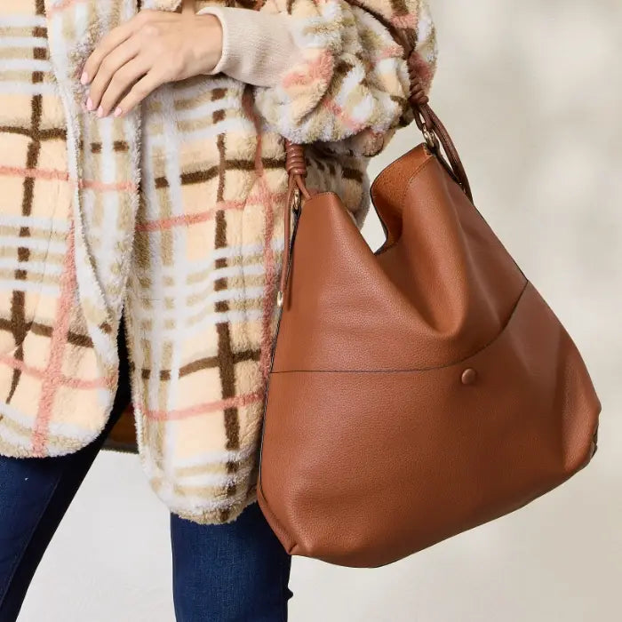 Woman holding brown handbag with coiled handle wearing plaid coat and jeans