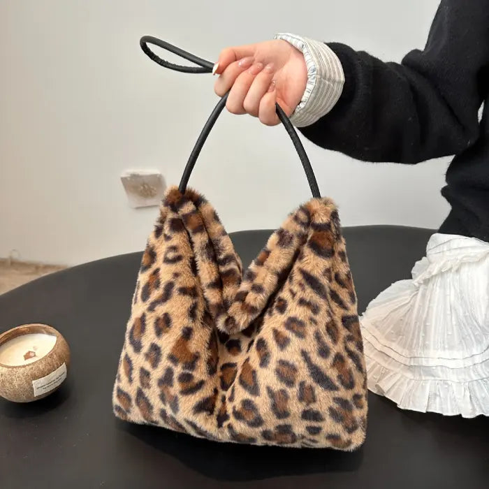 Brown leopard faux fur handbag with black strap, placed on a table for a modern stylish accessory.