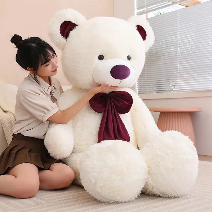 Two large teddy bears with bows, pink and brown, sitting on a sofa.