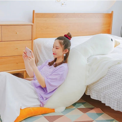 Young woman relaxing on a large white duck-shaped pillow in bedroom.