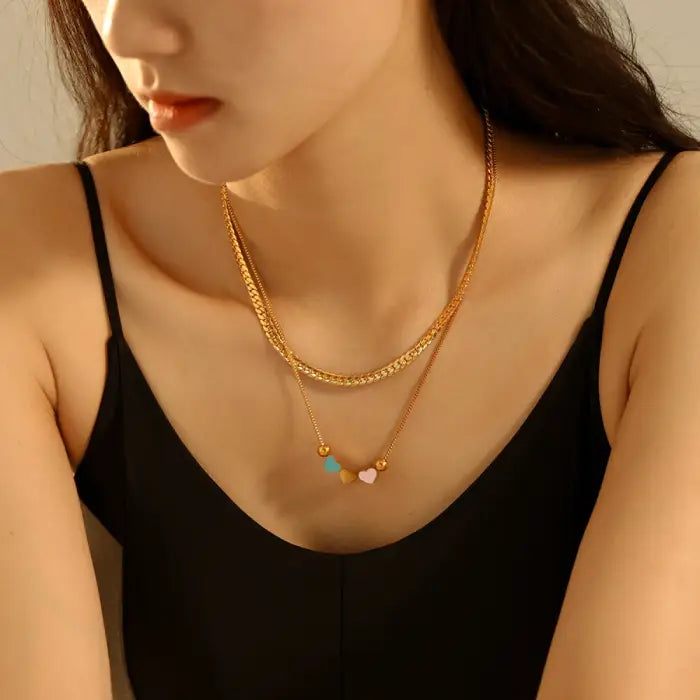 A woman wearing a black top and a gold necklace with small heart pendants in blue, yellow, and pink.