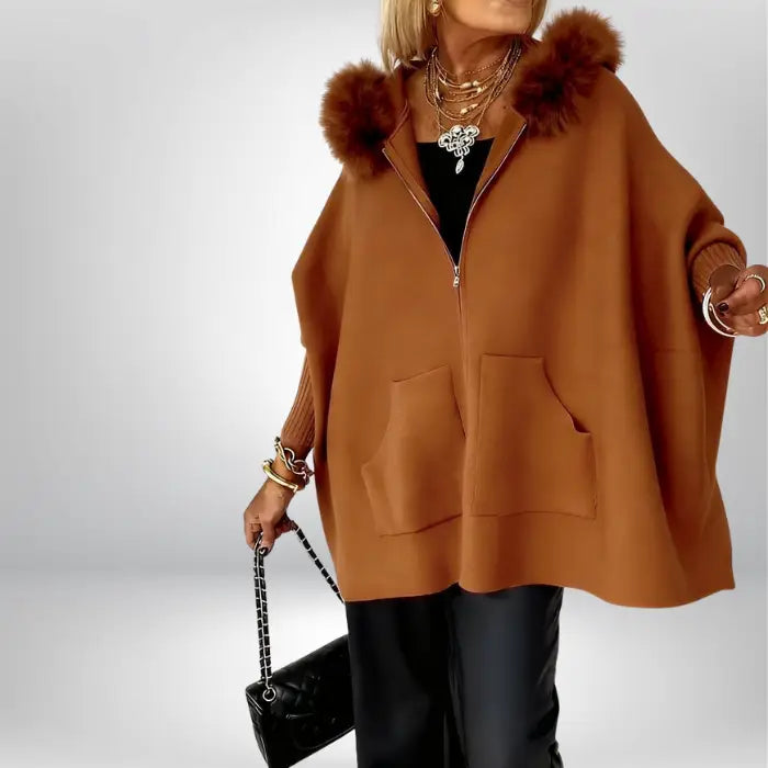 Women’s cape coat in warm brown with fur hood and oversized silhouette, styled with layered jewelry for classic seasonal elegance