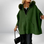 Women’s cape coat in deep green featuring plush fur hood and wide draped fit, creating warm sophisticated style for cool-weather looks