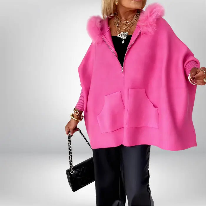 Women’s cape coat in bright pink with fur hood and pockets, dramatic draped shape offering warm trendy comfort for winter outfits