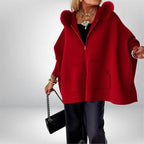 Women’s cape coat in bold red with soft fur hood and oversized drape, paired with jewelry for a refined standout winter outerwear look