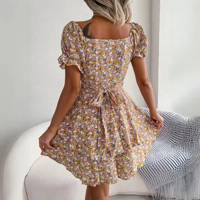 Women’s flower print mini dress back view showing waist tie and puff sleeves in a vibrant yellow floral pattern.
