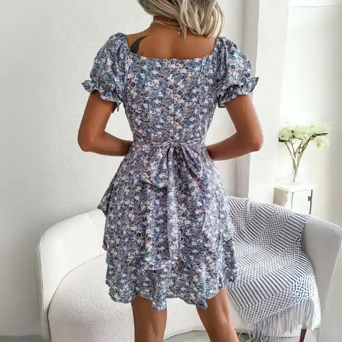 Women's flower print mini dress in blue back view with bow tie at waist and gathered bodice.