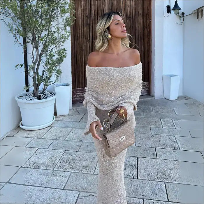  Women's one-shoulder long-sleeve knitted vacation dress in beige styled outdoors with gold accents.