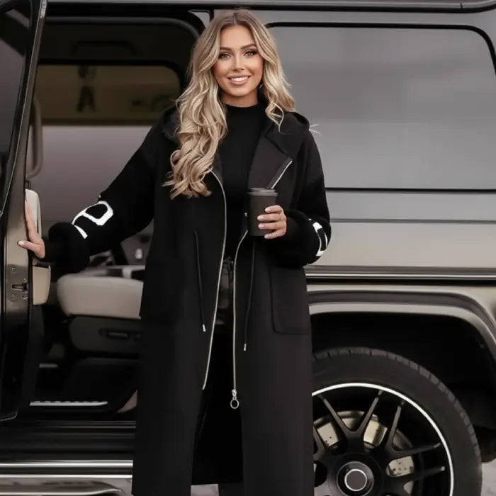 Women’s long hooded cardigan coat in black styled outdoors near vehicle, sleek knit sleeves offering elegant modern outerwear comfort